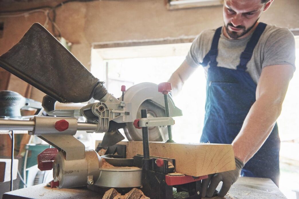 A beautifully arranged woodworking shop featuring a table saw and miter saw, illuminated by sunlight.