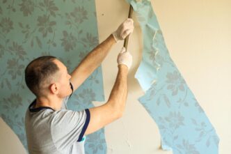 Homeowner peeling vintage wallpaper, revealing textured wall surfaces in soft, natural light.